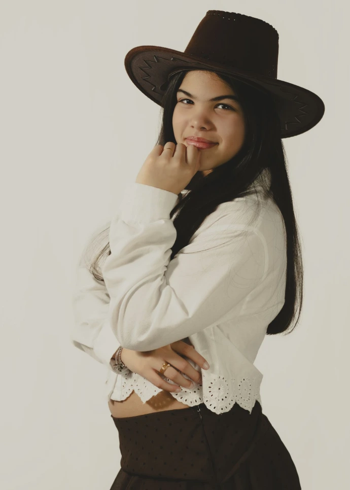 Retrato con Estilo y Sombrero Vaquero, Fotografía de plano medio con una iluminación clara que resalta el vestuario y el sombrero de la modelo. La pose es profesional y sencilla, centrando la atención en la expresión personal.