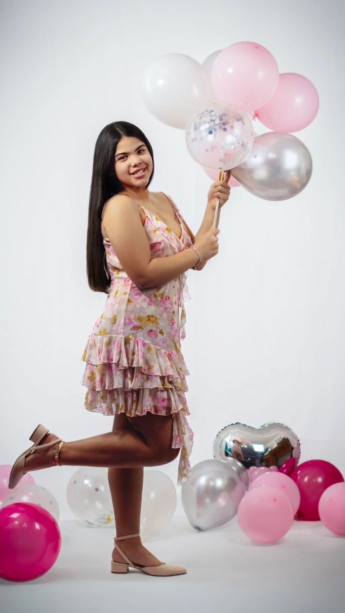 Fotografía de Estudio con Globos, captura de cuerpo completo que muestra a una joven sosteniendo un ramo de globos en una pose dinámica. El suelo del estudio está decorado con globos de diversos colores que complementan la composición