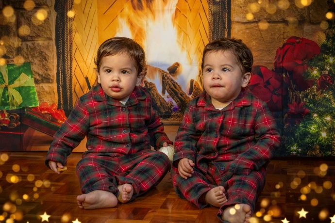 "Primer plano de dos niños varones en Navidad, posando con expresiones muy divertidas y juguetonas. Visten pijamas de Sherlock idénticos. La foto captura un momento de complicidad y diversión entre hermanos."