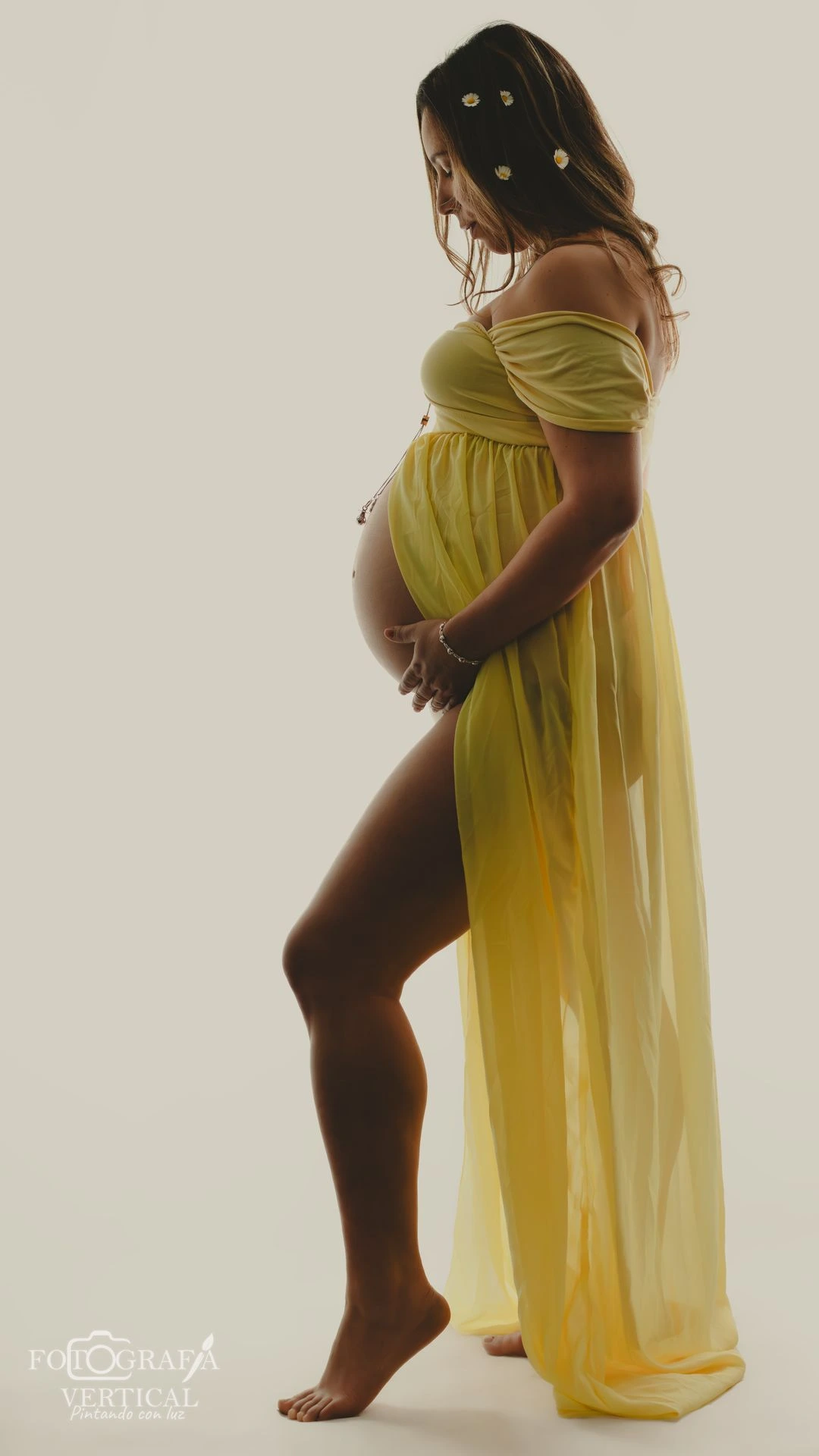 Retrato de perfil de mujer embarazada con vestido largo amarillo y flores resaltando la belleza de su silueta.